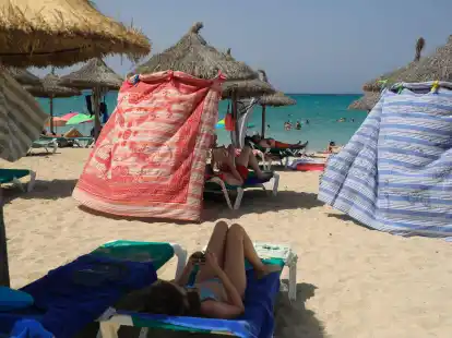 Menschen sch&uuml;tzen sich bei extremer Hitze mit Strandt&uuml;chern vor der Sonne am Strand von Arenal.