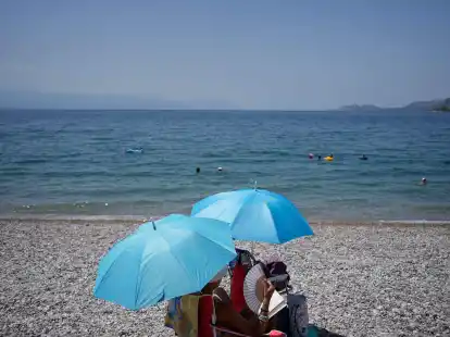 Da helfen nur noch Sonnenschrirme und ein Handventilator:&nbsp;Eine Frau am Strand von Loutraki.