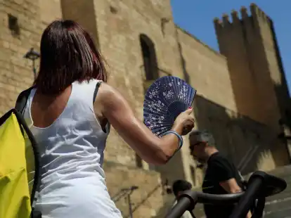 Eine Frau mit einem F&auml;cher geht bei gro&szlig;er Hitze durch die Innenstadt von Palma.