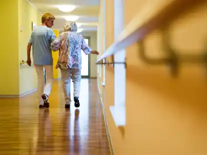 Eine Pflegerin geht in einem Pflegeheim mit einer &auml;lteren Dame &uuml;ber einen Korridor. Der Eigenanteil f&uuml;r einen Heimplatz ist in Niedersachsen im Durchschnitt um 406 Euro gestiegen.