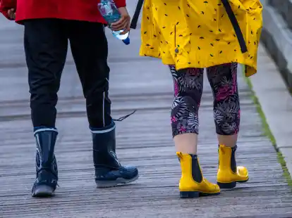Mit Gummistiefeln sind Urlauber bei starkem Regen unterwegs. K&uuml;hl und regnerisch zeigt sich das Wetter derzeit in Norddeutschland.