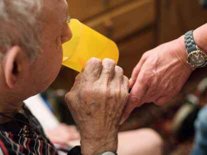 Eine ambulante Pflegerin hilft einem alten Mann bei der Tabletteneinnahme.