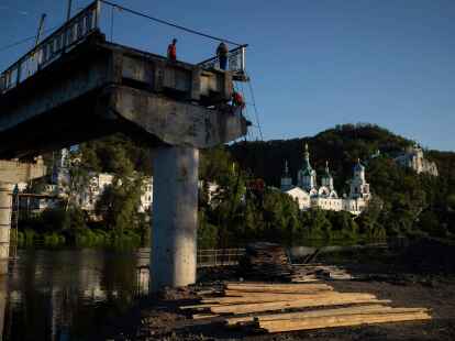 Bauarbeiter steigen von einer Leiter auf einer zerst&ouml;rten Br&uuml;cke neben dem Kloster Swjatohirsk herunter.