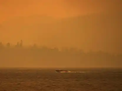 Ein Boot f&auml;hrt auf dem Okanagan-See, w&auml;hrend der Rauch des McDougall-Creek-Wildfeuers &uuml;ber dem Gebiet liegt.