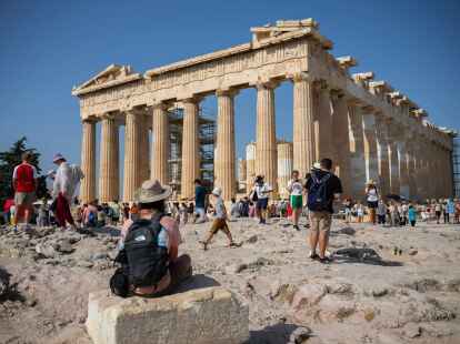 Touristen in Athen gehen an einem hei&szlig;en Tag bei ihrem Besuch des Parthenon-Tempels auf dem Akropolis-H&uuml;gel.