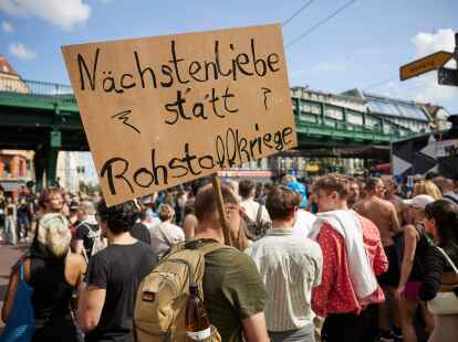 Ein Feiernder tr&auml;gt ein Schild mit der Aufschrift &laquo;N&auml;chstenliebe statt Rohstoffkriege&raquo; bei der Technoparade Zug der Liebe durch Berlin.
