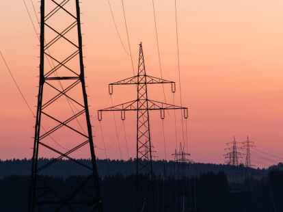 Strommasten sind bei Sonnenaufgang als Silhouette zu sehen.