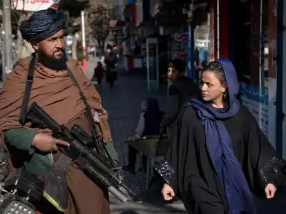 Ein Taliban-K&auml;mpfer steht in Kabul Wache, w&auml;hrend eine Frau vorbeil&auml;uft. (Archivbild)