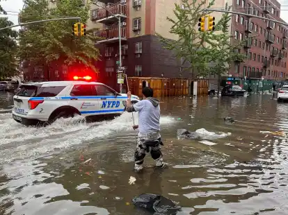 Hochwasser auf den Stra&szlig;en von New York: Im Stadtteil Brooklyn versucht ein Mann, mit einem  Stock einen Abfluss zu reinigen, w&auml;hrend ein Polizeiwagen vorbeif&auml;hrt.