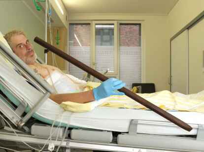 Patient Frank Vaorin liegt im Krankenhausbett und h&auml;lt die Zaunstange in der Hand, die seinen K&ouml;rper durchbohrte.