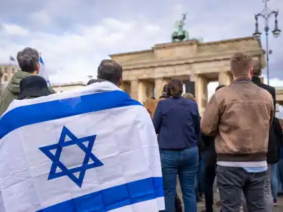 Teilnehmer der Kundgebung &bdquo;Aufstehen gegen Terror, Hass und Antisemitismus &ndash; in Solidarit&auml;t und Mitgef&uuml;hl mit Israel&ldquo; stehen umh&uuml;llt in eine israelische Flagge vor dem Brandenburger Tor in Berlin.