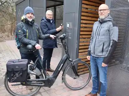 Demonstrieren die Nutzung der Sammelschlie&szlig;anlage am Bahnhof in Gro&szlig;enkneten: B&uuml;rgermeister Thorsten Schmidtke (Mitte) scannt mit dem Smartphone den QR-Code an der Anlage, Arne Kunz (links) schiebt das Fahrrad ins Innere der Anlage, an dessen Realisierung Wilko Jan&szlig;en beteiligt war.