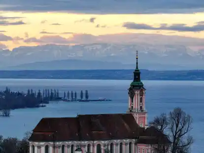 Hinter der ehemaligen Klosterkirche Birnau am Bodensee geht die Sonne auf. Die Alpen sind im Hintergrund zu sehen.