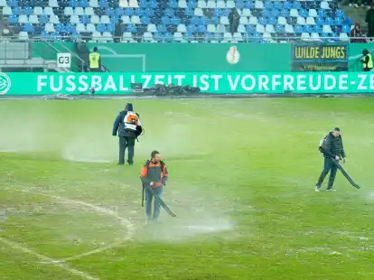 Arbeiter versuchten, Wasserlachen vom Spielfeld im Ludwigsparkstadion zu entfernen.