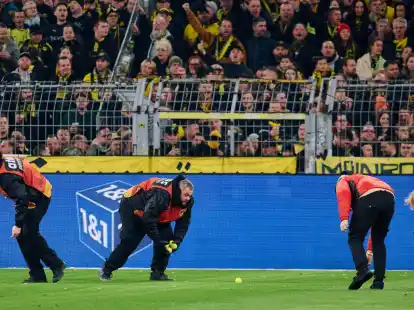 Stadionmitarbeiter sammeln Tennisb&auml;lle ein, die Fans auf das Spielfeld geworfen haben, um gegen Investoren in der DFL zu protestieren.
