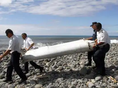 Techniker tragen ein Wrackteil, die Fl&uuml;gelklappe eines Flugzeugs, &uuml;ber einen Strand bei Saint-Andr&eacute;,  R&eacute;union.