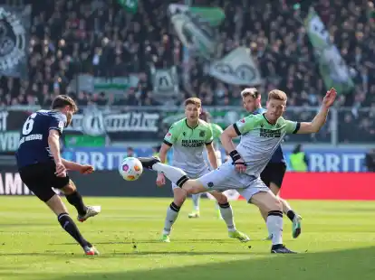 Gino Fechner (l) vom SV Wehen Wiesbaden zieht ab. Hannovers Marcel Halstenberg (r) versucht den Ball zu blocken.