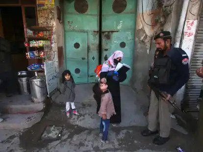 Ein Polizist in Pakistan steht Wache, w&auml;hrend einem Kind ein Polio-Impfstoff verabreicht wird.
