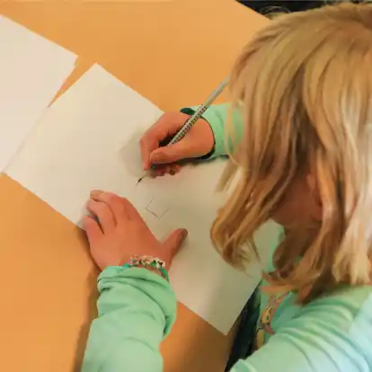 Ein Kind zeichnet ein auf einem Zettel abgebildetes Kreuz ab. In Niedersachsen werden bei Schuleingangsuntersuchungen immer mehr sprachliche Defizite festgestellt.