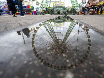 Ein Riesenrad spiegelt sich in einer Pfütze auf dem Festgelände des Stuttgarter Frühlingsfestes.