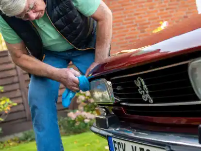 Ein Mann reinigt die Scheinwerfer seines Peugeot 504 Coupé-Oldtimers. Unter Umständen kann man das Licht auf modernes LED-Licht aufrüsten, ohne den Oldtimerstatus zu verlieren.
