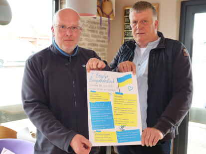 Frank Schwalm (links) und Ralf Meyer präsentieren das Plakat, mit dem die Ukraine-Hilfe Bösel zum 1. Bürgerfrühstück in den Dorfpark ein.