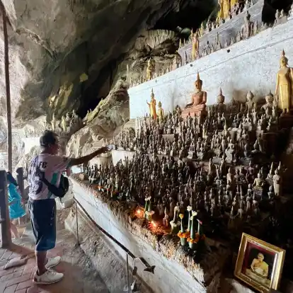 Ein Mann besprenkelt Buddha-Statuen in den Pak Ou Caves als Zeichen des tiefen Respekts mit Wasser.