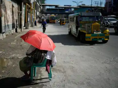 Eine Straßenverkäuferin schützt sich in Manila mit einem Regenschirm vor der Sonne.
