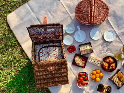 So sieht wohl ein klassisches Picknick aus: leckere Snacks aus dem Picknickkorb, die man auf der Picknickdecke sitzend genießt.
