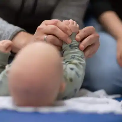 Ein Vater hält während eines Infant Handling Kurses die Füße seines Kindes, während die Mutter daneben sitzt.