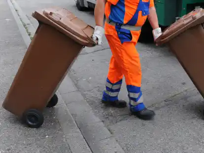 Ein Mitarbeiter der Abfallwirtschaft  schiebt eine braune Tonne mit Biomüll zum Müllwagen.