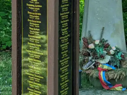Auf dem Friedhof II in Blexen erinnern Stelen und ein steinernes Kreuz an Kriegsgefangene, die während der Nazi-Herrschaft in Nordenham ums Leben gekommen sind. Im Hintergrund: ein vertrockneter Kranz der Stadt Nordenham