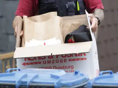 Ein Polizist trägt nach einer Wohnungsdurchsuchung einen Karton mit sichergestellte Gegenständen.