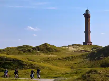 Idylle pur: der große Norderneyer Leuchtturm und ein Fahrradweg in der Dünenlandschaft.
