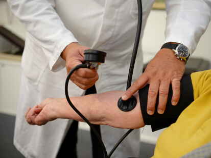 Ein Hausarzt misst  einer Patientin den Blutdruck.