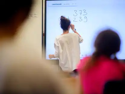 Eine Lehrerin schreibt eine Mathematikaufgabe auf eine digitale Schultafel im Klassenraum einer 4. Klasse einer Grundschule.