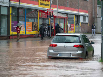 Passanten stapfen und fahren durch das Hochwasser in der Fischbachstrasse in Saarbrücken. Nach starken Regenfällen steht diese teilweise unter Wasser.