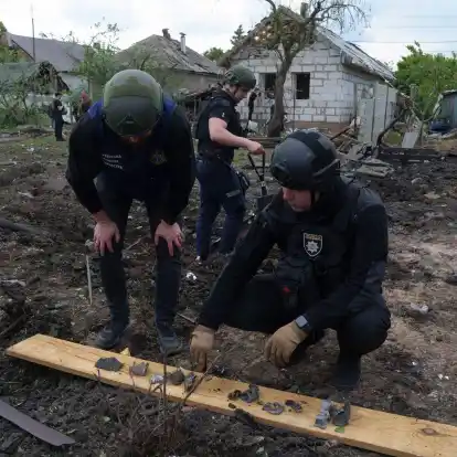 Ein ukrainischer Polizeibeamter und ein Staatsanwalt für Kriegsverbrechen inspizieren Bruchstücke einer Gleitbombe vor einem beschädigten Haus nach einem russischen Luftangriff auf ein Wohnviertel.