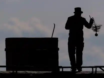 Ein Schornsteinfeger mit seinem Kaminkehrerwerkzeug auf einem Dach.