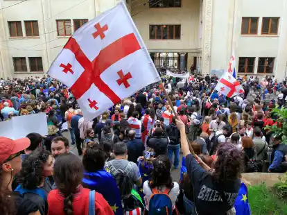 Demonstrantinnen und Demonstranten schwenken vor dem Parlamentsgebäude in Tiflis georgische Nationalflaggen.
