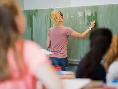 Eine junge Lehrerin schreibt Mathematikaufgaben an eine Schultafel. Niedersachsen will 390 Schulen im Land nach Sozialindex stärker fördern.