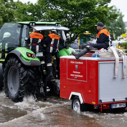 Feuerwehrleute fahren in Reichertshofen über einr überflutete Straße.