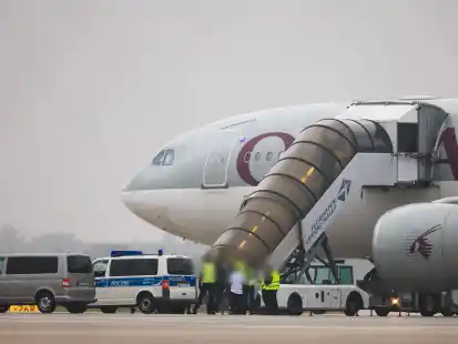 Menschen besteigen ein Flugzeug der Qatar Airways, vor dem Fahrzeuge der Bundespolizei stehen auf dem Vorfeld am Flughafen Leipzig/Halle.