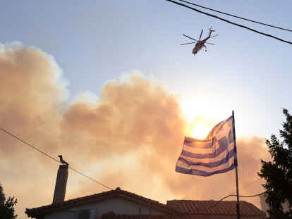 Ein Hubschrauber fliegt über ein brennendes Gebiet während eines Waldbrandes im nordwestlichen Vorort Kryoneri.