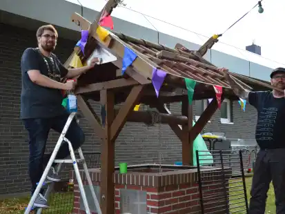Kevin Keil (links) als scheidender und Hajo Freese als neuer Brunnenmeister putzen und schm&uuml;cken den Brunnen neben der ehemaligen Volksbank.
