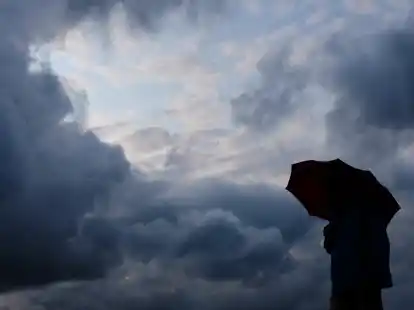 Ein Mann geht mit einem Regenschirm vor aufziehenden dunklen Wolken spazieren. (Symbolbild)